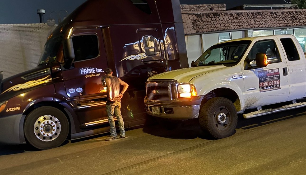 Cameron working on a semi truck at night with the Freedom service truck nose to nose