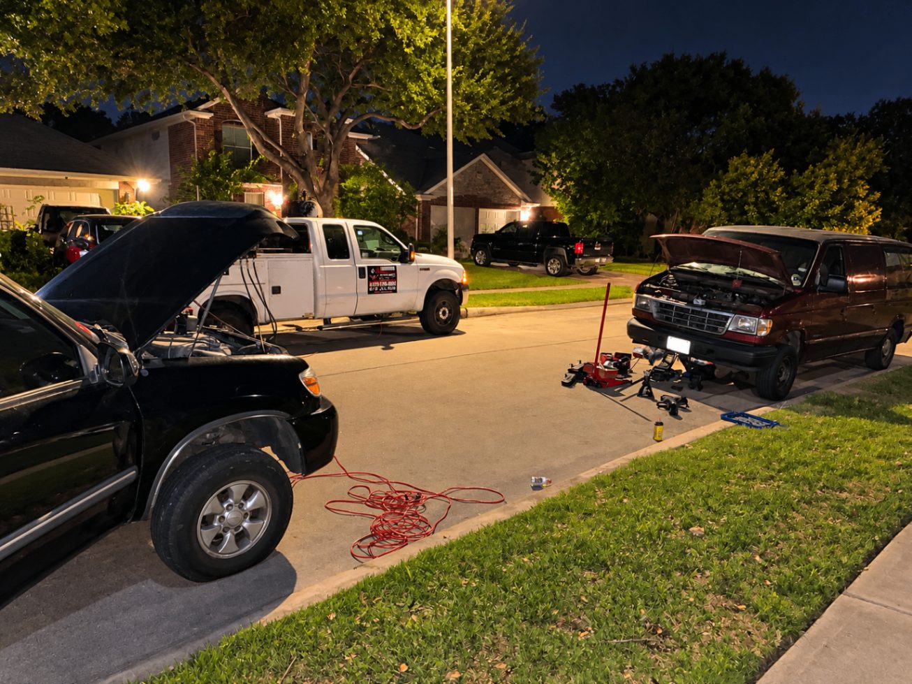 Two vehicles worked on at once on a residential street at night, service truck behind