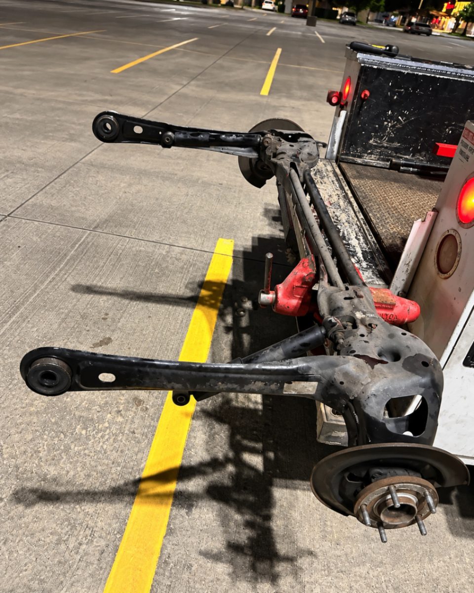Rear subframe and trailing arms removed and set on the service truck tailgate in a parking lot at night